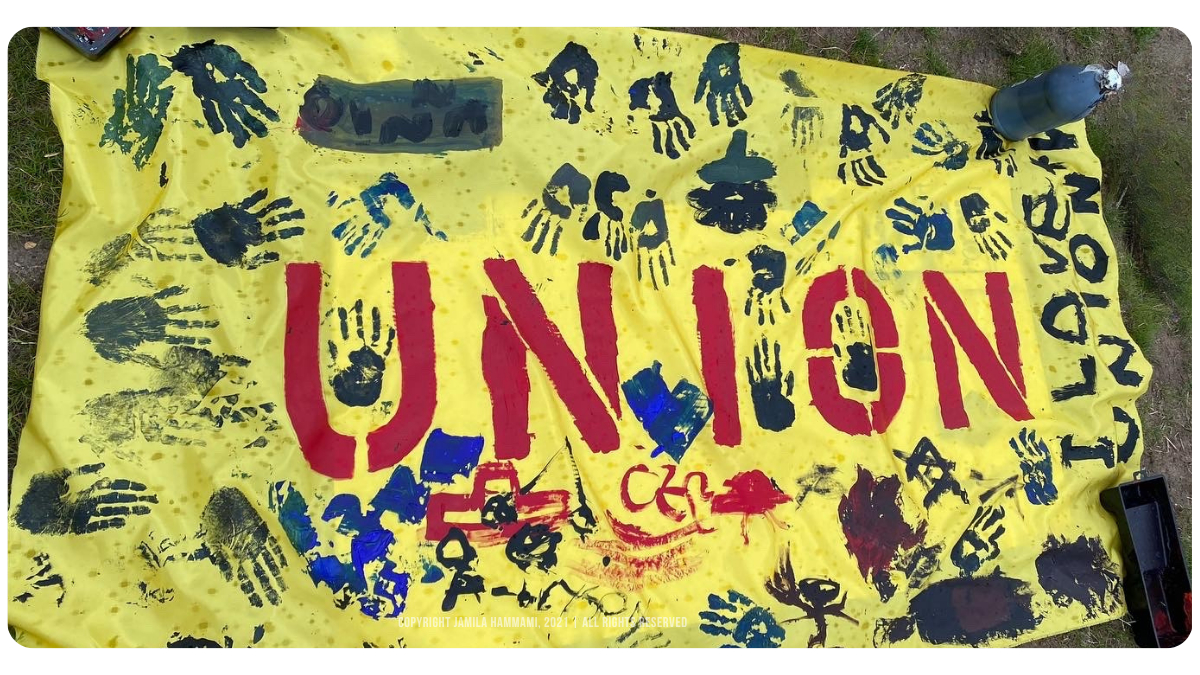 Finger-painted “Union” banner by Amazon Labor Union (ALU) workers’ children, outside of Amazon’s Staten Island JFK8 fulfillment center, New York, July 2021 | Photo Credit & Copyright: Jamila Hammami, 2021. | All Rights Reserved.